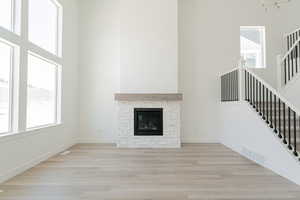 Unfurnished living room featuring a stone fireplace, light wood-type flooring, and a wealth of natural light