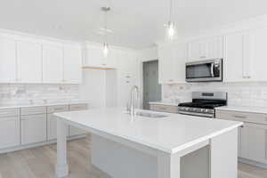 Kitchen featuring backsplash, appliances with stainless steel finishes, a center island with sink, and light hardwood / wood-style floors