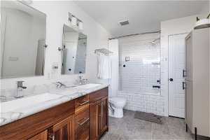 Full bathroom featuring dual bowl vanity, toilet, shower / bath combo with shower curtain, and tile floors