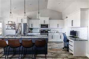 Kitchen featuring dark hardwood / wood-style floors, white cabinetry, pendant lighting, tasteful backsplash, and appliances with stainless steel finishes