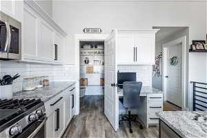 Kitchen featuring white cabinets, stainless steel appliances, light hardwood / wood-style floors, and light stone counters