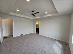 Spare room with a raised ceiling, ceiling fan, and carpet
