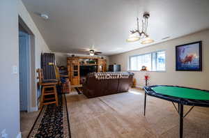 Playroom featuring ceiling fan with notable chandelier, light colored carpet, and a textured ceiling