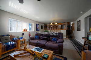 Living room featuring ceiling fan with notable chandelier and carpet flooring