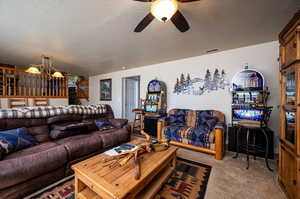 Carpeted living room featuring ceiling fan with notable chandelier and a textured ceiling