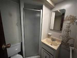 Bathroom featuring vanity with extensive cabinet space, a shower with door, and toilet