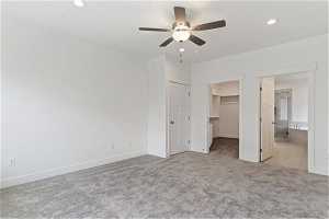 Unfurnished bedroom featuring a walk in closet, a closet, light carpet, and ceiling fan