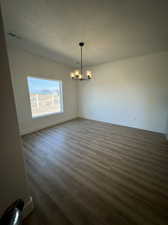 Unfurnished room featuring dark hardwood / wood-style floors, a chandelier, and a textured ceiling