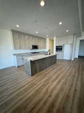 Kitchen with stainless steel appliances, hardwood / wood-style floors, sink, light stone counters, and a kitchen island with sink
