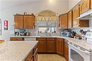 Kitchen featuring sink, white appliances, lofted ceiling, light tile floors, and backsplash