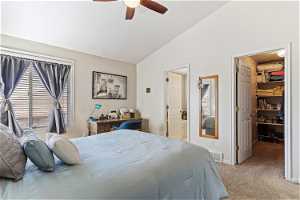 Carpeted bedroom featuring vaulted ceiling, a walk in closet, ensuite bath, and ceiling fan