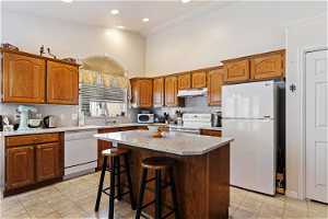 Kitchen with tasteful backsplash, white appliances, light tile flooring, sink, and a center island