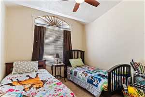 Bedroom with a textured ceiling, vaulted ceiling, carpet flooring, and ceiling fan