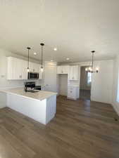 Kitchen with appliances with stainless steel finishes, dark hardwood / wood-style floors, a textured ceiling, white cabinets, and decorative light fixtures.  Pictures are for reference only of the MAINE floor plan. Actual finishes may vary.