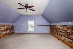 Additional living space with brick wall, vaulted ceiling, ceiling fan, and carpet flooring