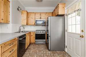 Kitchen with light tile floors, sink, tasteful backsplash, stainless steel appliances, and ornamental molding