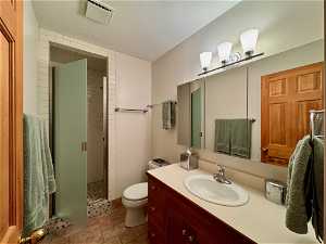 upper 3/4 Bathroom featuring vanity with extensive cabinet space, a textured ceiling, toilet, tile floors, and a tile shower
