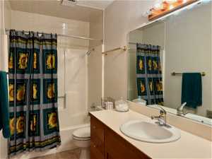 Main floor Full bathroom with toilet, vanity with extensive cabinet space, tile flooring, and shower / tub combo with curtain