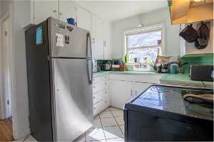Kitchen featuring light tile floors, stainless steel fridge, white cabinetry, and sink