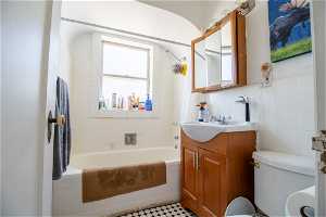 Full bathroom featuring tiled shower / bath, tile walls, tile floors, vanity, and toilet