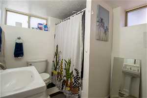 Bathroom featuring a textured ceiling, toilet, and sink
