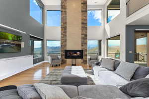 Living room featuring light wood-type flooring, a fireplace, a towering ceiling, and a healthy amount of sunlight