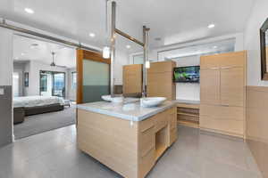 Kitchen with light tile flooring, a kitchen island with sink, sink, light stone countertops, and ceiling fan