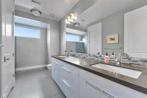 Bathroom featuring dual vanity, toilet, tasteful backsplash, and tile flooring