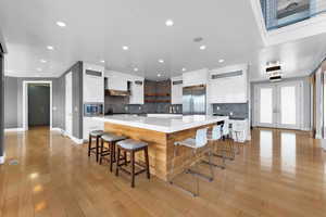 Kitchen featuring wall chimney range hood, white cabinetry, french doors, built in appliances, and a kitchen bar