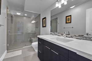 Bathroom featuring vanity with extensive cabinet space, tasteful backsplash, toilet, tile floors, and a shower with shower door