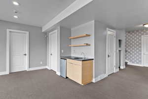 Kitchen featuring stainless steel dishwasher, dark carpet, sink, and light brown cabinets