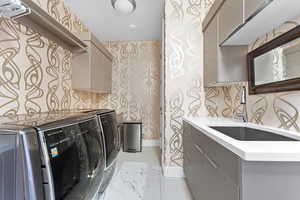 Clothes washing area with light tile floors, cabinets, sink, and washing machine and clothes dryer