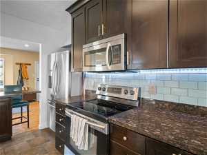 Kitchen with tasteful backsplash, stainless steel appliances, dark brown cabinets, and dark tile flooring