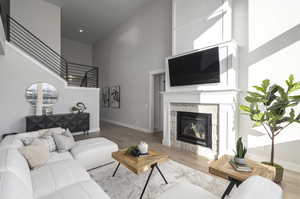 Living room featuring a towering ceiling, a tiled fireplace, and light hardwood / wood-style flooring