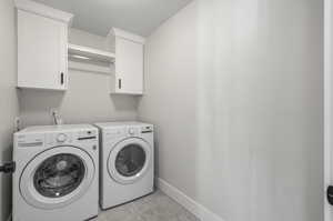 Laundry room featuring independent washer and dryer, light tile floors, and cabinets