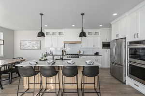 Kitchen featuring backsplash, white cabinets, stainless steel appliances, hardwood / wood-style floors, and hanging light fixtures