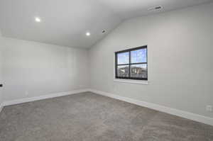 Carpeted spare room featuring vaulted ceiling