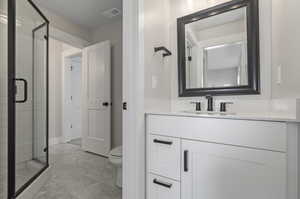 Bathroom featuring a shower with door, toilet, and vanity