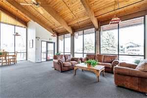 Carpeted living room featuring wooden ceiling, a wealth of natural light, beam ceiling, and ceiling fan