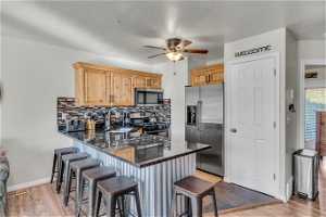 Kitchen with light wood-type flooring, kitchen peninsula, ceiling fan, stainless steel appliances, and a breakfast bar