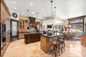 Kitchen with hanging light fixtures, appliances with stainless steel finishes, an island with sink, and custom range hood