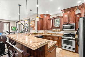 Kitchen with light tile floors, sink, hanging light fixtures, appliances with stainless steel finishes, and a kitchen bar