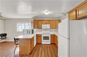 Apartment kitchen with a breakfast bar, white appliances, and light hardwood / wood-style floors
