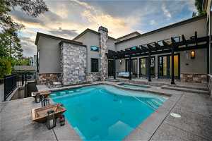 Pool at dusk with a patio area, an in ground hot tub, and a pergola