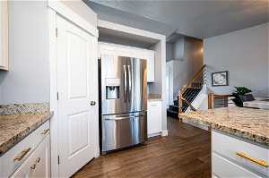 Kitchen featuring white cabinetry, light stone countertops, dark hardwood / wood-style floors, and stainless steel fridge with ice dispenser