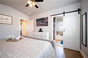 Bedroom featuring a barn door, ensuite bathroom, lofted ceiling, ceiling fan, and light hardwood / wood-style floors