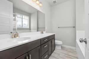 Bathroom with a bathtub, vanity with extensive cabinet space, dual sinks, toilet, and wood-type flooring