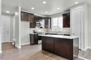 Kitchen with appliances with stainless steel finishes, dark brown cabinetry, a center island, tasteful backsplash, and wood-type flooring