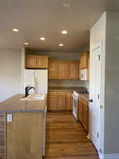 Kitchen featuring sink, an island with sink, white appliances, and dark hardwood / wood-style flooring