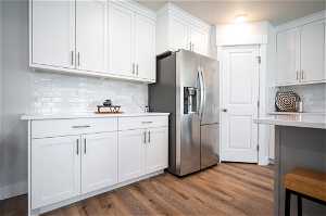 Kitchen featuring tasteful backsplash, stainless steel refrigerator with ice dispenser, white cabinets, and hardwood / wood-style floors